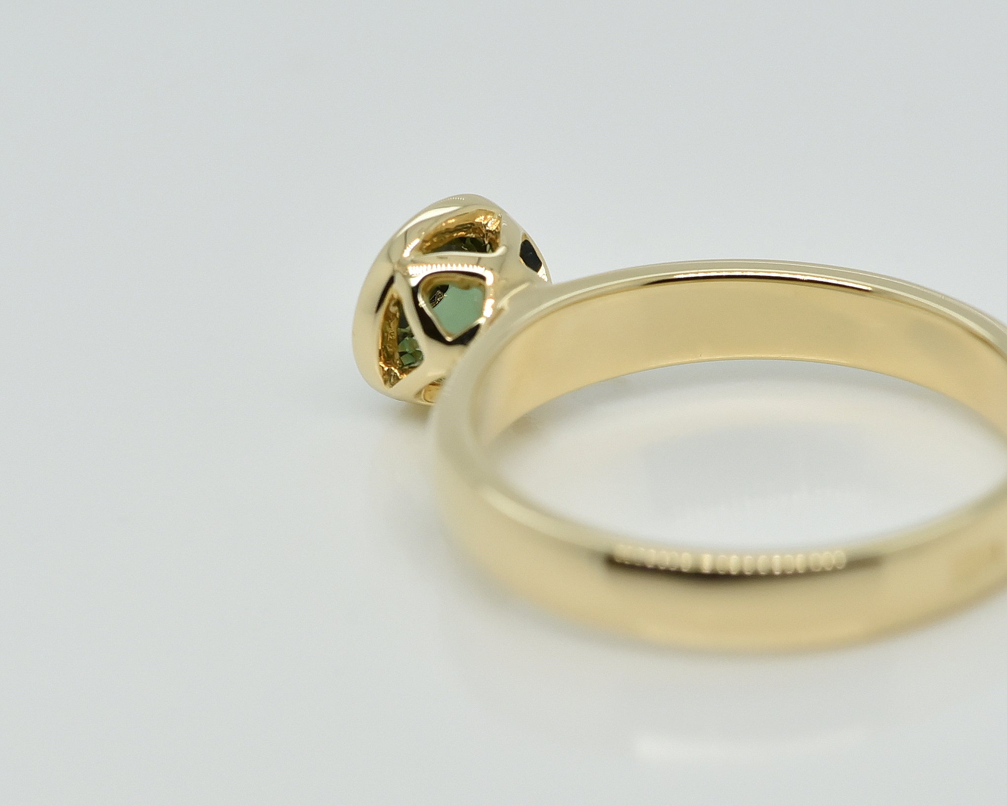 Geltono aukso žiedas su ažūrine karūnėle baltame fone iš galo